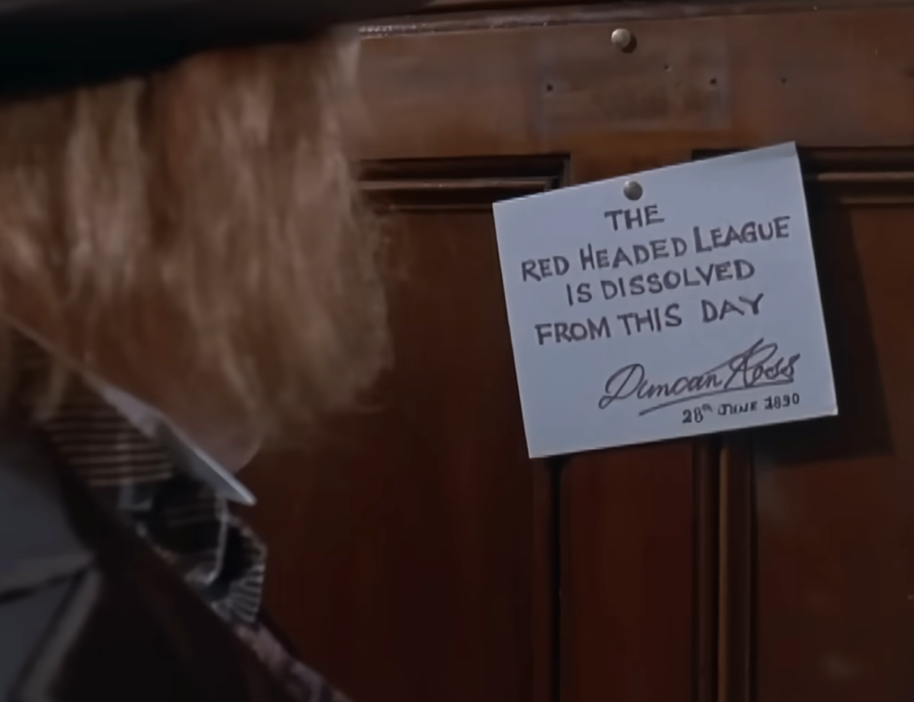 Close-up of a notice on a wooden door reading 'THE RED HEADED LEAGUE IS DISSOLVED FROM THIS DAY' signed by Duncan Ross, dated 9th June 1890